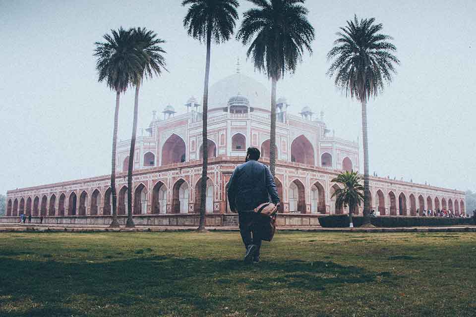 A man in the foreground walks toward Humayun's Tomb, partially shrouded in fog, in New Delhi