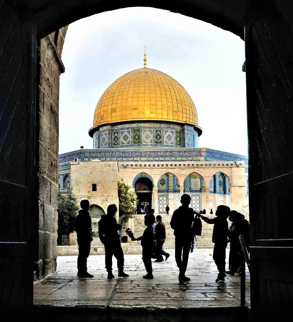 A photograph of a number of children standing in shadow in an archway that opens to the Dome of the Rock