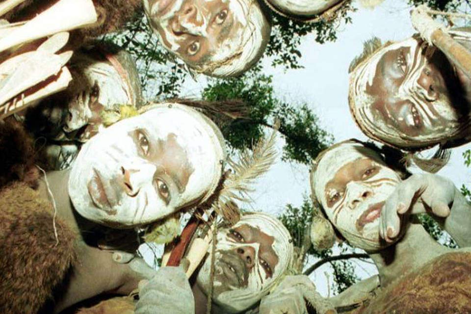 A photograph taken from below looking up at a circle of indigenous faces looking down