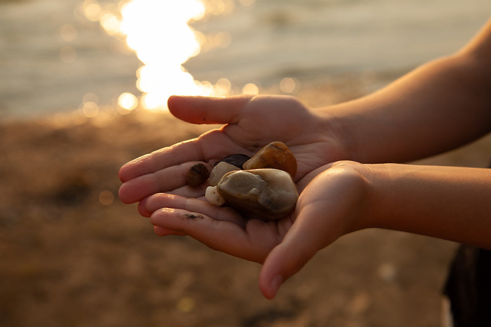 A photograph of a pair of hands holding out a small pile of pebbles on a beach