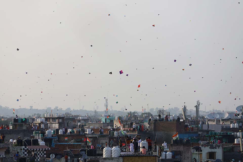 A distant shot of a cityscape. Kites dot the sky are rising into the air.