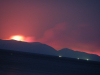 A photograph of a landscape at night, a fire burning ominously behind a hill in the background