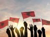 A photograph of hands waving small flags at sunset