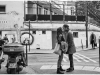 A black and white photograph of a man and a woman kissing in on a busy city street