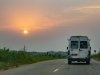 A photograph from behind of a van driving away into the sunset