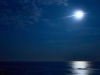 A photograph of a look out at sea, where the moon, just wrapped in gauzy clouds, hovers over a motionless sea below