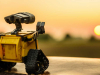 A photograph of a toy robot with a setting sun in the background