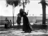 A grainy black and white photo of a woman in a long dress swaying at the waist with her hands up by her face