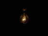 A photograph of a very dim lightbulb that is all but being swallowed by the darkness surrounding