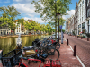 A photograph of a row of bikes parked by a canal that runs parallel to a picturesque city street in Amsterdam