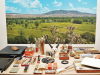 A table full of painting tools with a painting of a New Mexican landscape mounted on the wall behind it