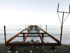 The steel frame of a dock, not covered and thus exposing the sea below, extends out from a rocky beach.