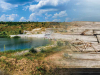 A digital collage. A photograph of a lake bordered by a rocky ridge that blends into a photograph of a worn-wooden raft.