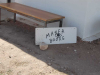 A photograph of a hand-lettered sign propped up against a low wooden bench. Text reads: Marfa Books