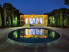 A photograph of an ornate building, lit up at night, which is also reflected in a pool in the courtyard