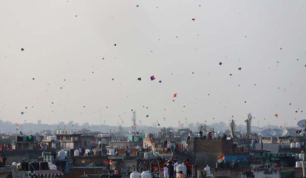 A distant shot of a cityscape. Kites dot the sky are rising into the air.