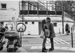 A black and white photograph of a man and a woman kissing in on a busy city street