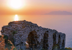 The remains of a stone arch perched on the edge of a cliff overlooking a sea