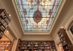 A photograph of the interior of Escaramuza looking up toward the intricate stained glass skylight