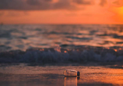 A photograph of a bottle overturned on a beach at sunset