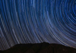 A time elapsed photo of the sky at night, the stars creating arcs of light across the sky