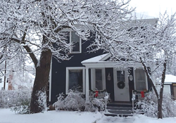 A blue house with snow on the roof and trees.